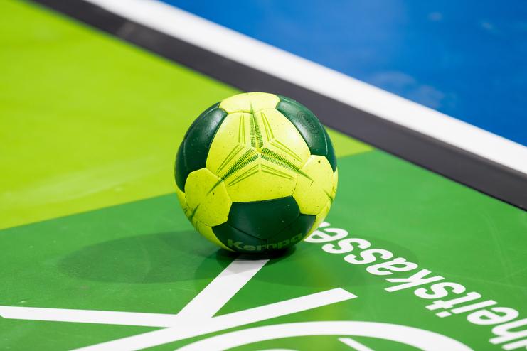 Grüner Handball auf einer grünen Sportfläche mit weißen Linien und einem blauen Hintergrund.