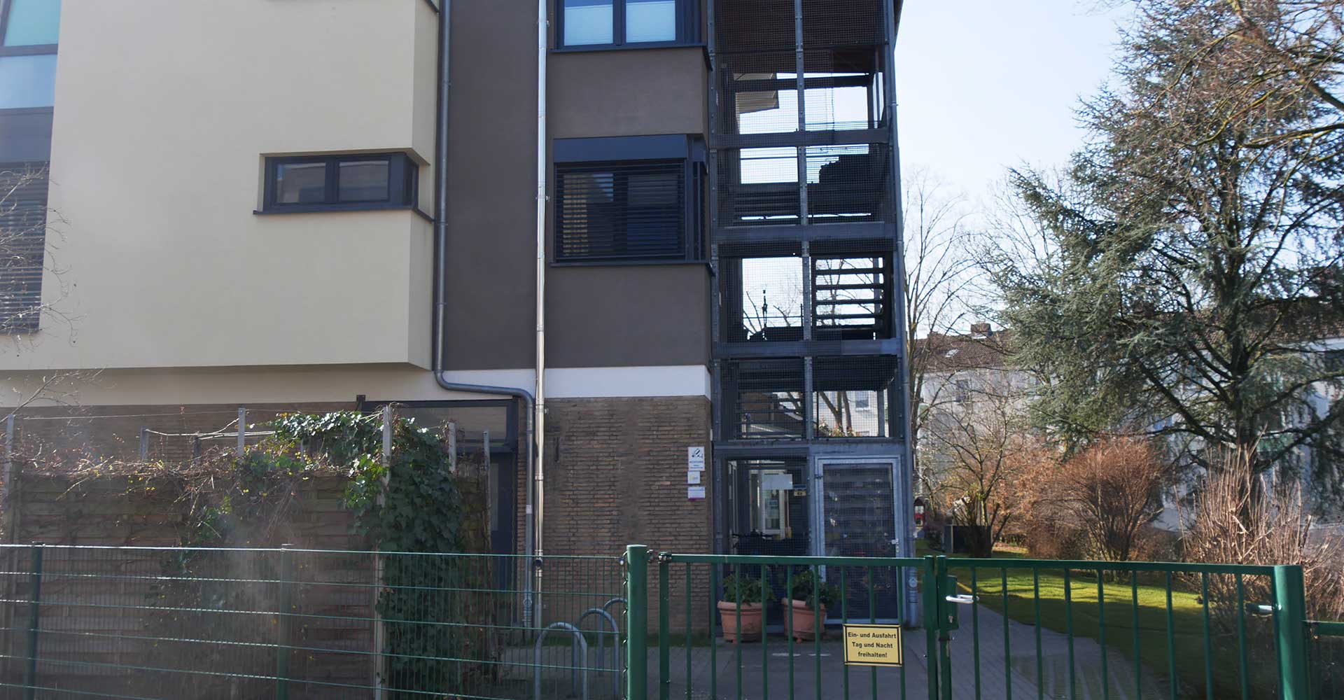 Moderne Wohngebäude mit Außentreppe, begrüntem Garten und Zugangstor in Tageslicht.